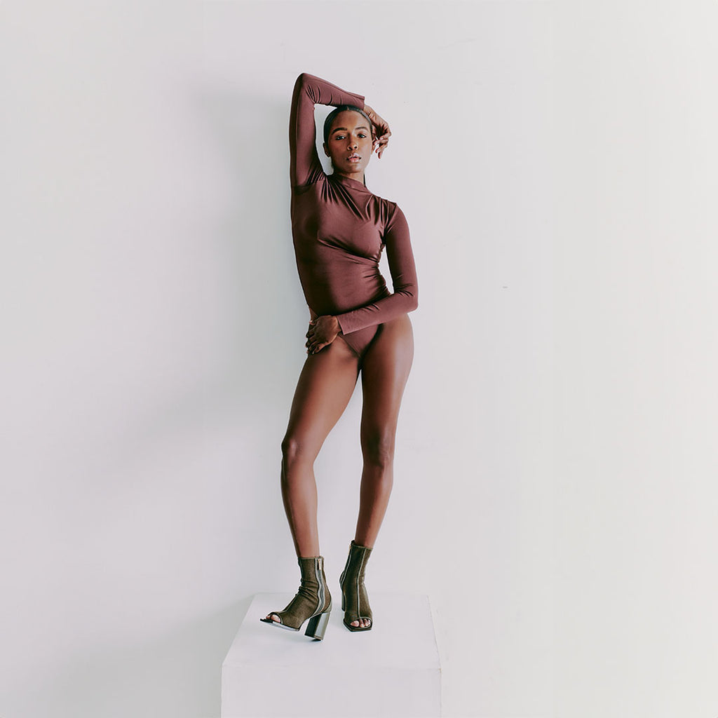 Model sitting in Daniella Shevel Onyx olive ankle boots paired with a simple, understated bodysuit for elegance.