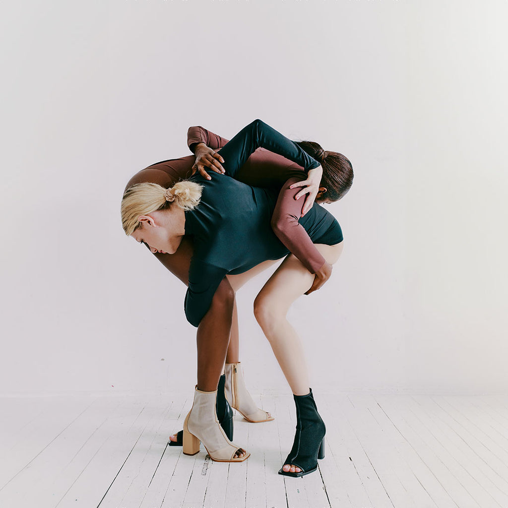 Two models wearing Daniella Shevel Onyx ankle boots in black and camel, showcasing versatile styling for every wardrobe. Wearing two neutral bodysuits